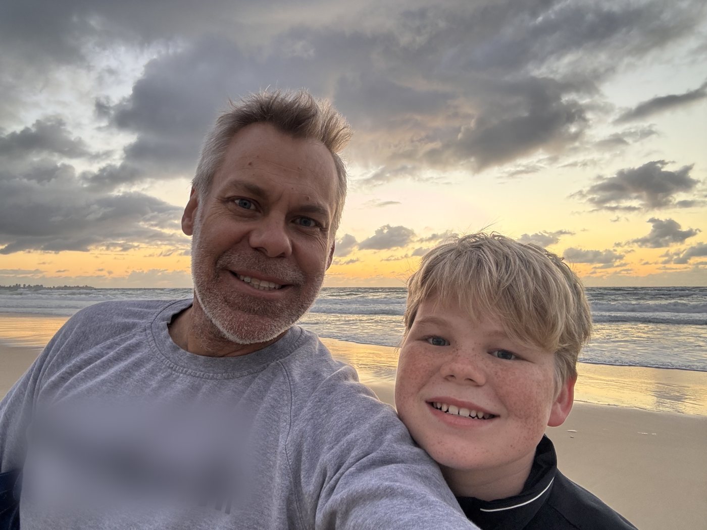 Marty and his son Rylan smiling together on the beach at sunrise